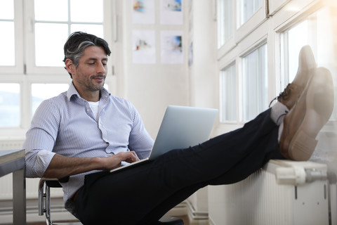 Man using laptop at the window in office stock photo