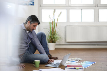 Mann mit Laptop auf dem Boden im Büro - FKF02211