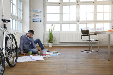 Man using laptop on the floor in a modern informal office - FKF02212