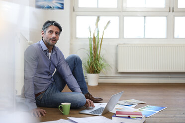 Mann mit Laptop auf dem Boden im Büro - FKF02213