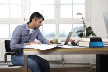 Man using laptop at desk in office - FKF02218