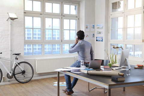 Ein Mann benutzt ein Mobiltelefon in einem modernen, informellen Büro, lizenzfreies Stockfoto