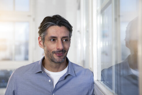 Lächelnder Mann im Büro schaut aus dem Fenster - FKF02226