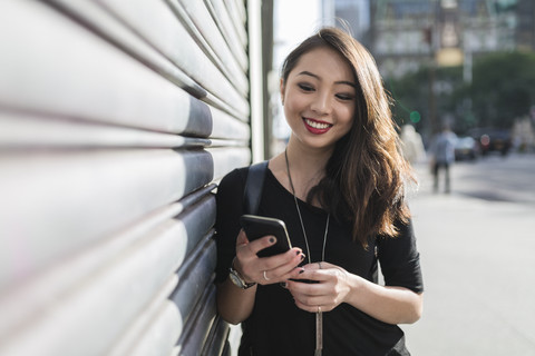 Porträt einer lächelnden jungen Frau, die auf ihr Mobiltelefon schaut, lizenzfreies Stockfoto