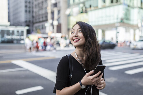 USA, New York City, Manhattan, young woman listening music with cell phone and earphones on the street - GIOF02489