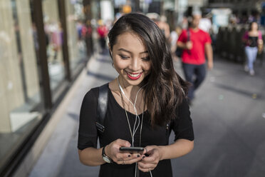 USA, New York City, Manhattan, junge Frau hört Musik mit Kopfhörern und schaut auf ihr Handy - GIOF02491