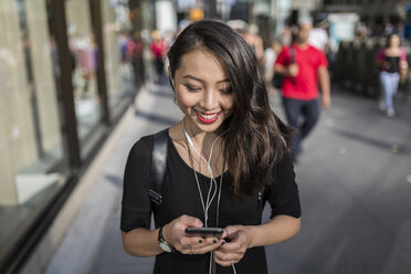 USA, New York City, Manhattan, young woman listening music with earphones while looking at cell phone - GIOF02491