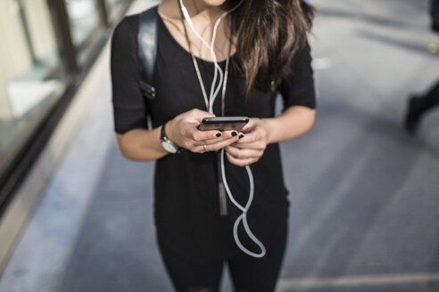 Junge Frau, die mit Kopfhörern Musik hört, während sie Textnachrichten schreibt, Teilansicht - GIOF02492