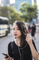 Portrait of young woman with earphones and cell phone watching something - GIOF02493