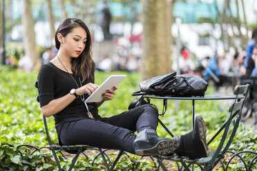 USA, New York, junge Frau sitzt im Stadtpark und benutzt ein Tablet - GIOF02500