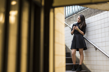 USA, New York City, Manhattan, young woman standing on stairs looking at smartphone - GIOF02504