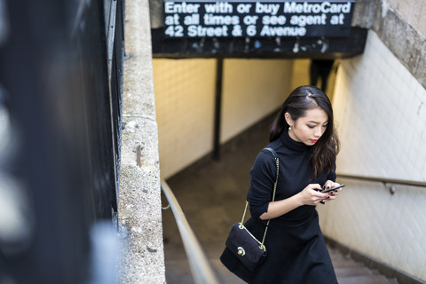 USA, New York City, Manhattan, junge Frau in Schwarz gekleidet, geht nach oben und schreibt eine SMS, lizenzfreies Stockfoto