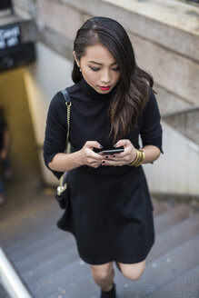 USA, New York City, Manhattan, junge Frau in Schwarz gekleidet, geht nach oben und schreibt eine SMS - GIOF02506