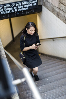 USA, New York City, Manhattan, junge, schwarz gekleidete Frau geht eine Treppe hinauf und schaut auf ihr Handy - GIOF02507