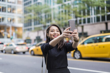 USA, New York City, Manhattan, Porträt einer lächelnden jungen Frau, die ein Selfie mit ihrem Smartphone macht - GIOF02509