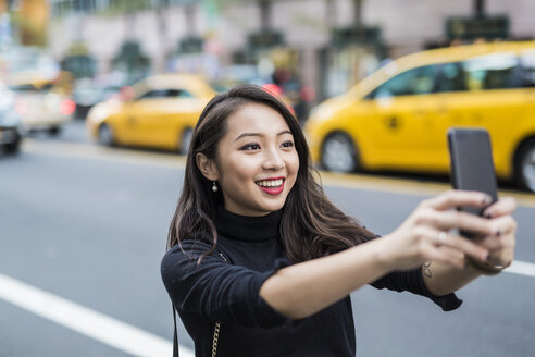 USA, New York City, Manhattan, portrait of smiling young woman taking selfie with smartphone - GIOF02510