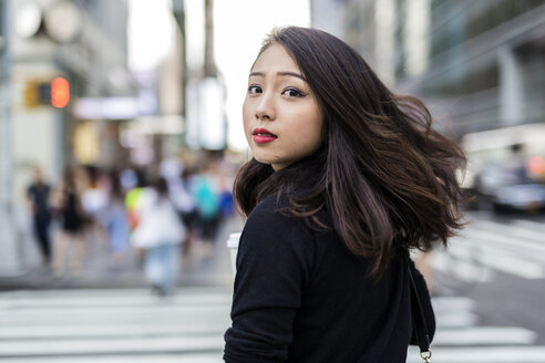 USA, New York City, Manhattan, Porträt einer jungen Frau, die beim Überqueren der Straße über ihre Schulter schaut - GIOF02514