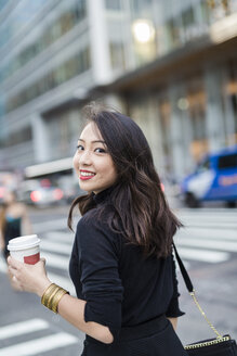 USA, New York City, Manhattan, Porträt einer lächelnden jungen Frau mit Kaffee zum Mitnehmen beim Überqueren der Straße - GIOF02516