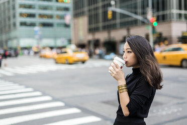 USA, New York City, Manhattan, junge Frau trinkt Kaffee zum Mitnehmen auf der Straße - GIOF02518