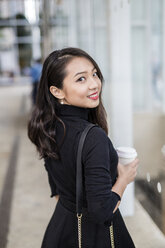 Porträt einer lächelnden jungen Frau mit Kaffee zum Mitnehmen, die über ihre Schulter schaut - GIOF02520