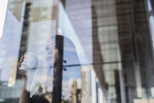 USA, New York City, Manhattan, junge Frau mit Kaffee zum Mitnehmen hinter Glasscheibe - GIOF02523