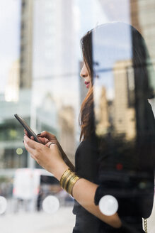USA, New York City, Manhattan, junge Frau hinter Glasscheibe schaut auf Handy - GIOF02524