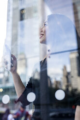 USA, New York City, Manhattan, smiling young woman behind glass pane watching something - GIOF02527