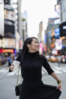 USA, New York City, Manhattan, junge Frau in Schwarz gekleidet mit Kaffee zum Mitnehmen auf der Straße - GIOF02533