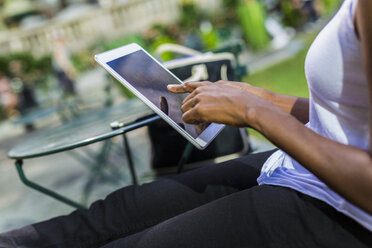 Frau sitzt in einem Park und benutzt ein Tablet, Teilansicht - GIOF02537