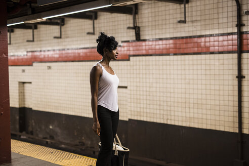 USA, New York City, Manhattan, Frau mit Einkaufstasche wartet am Bahnsteig einer U-Bahn-Station - GIOF02544