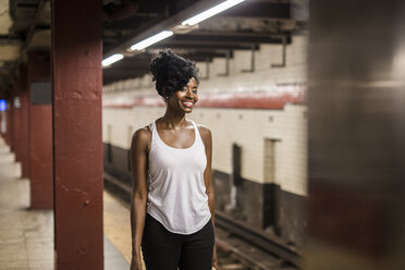 USA, New York City, Manhattan, lächelnde Frau wartet am Bahnsteig einer U-Bahn-Station - GIOF02545