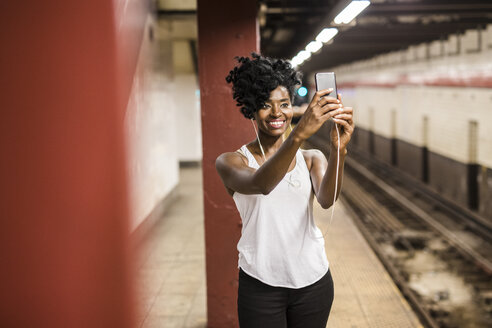 USA, New York City, Manhattan, lächelnde Frau, die ein Selfie am Bahnsteig einer U-Bahn-Station macht - GIOF02546