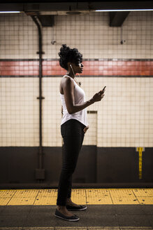 USA, New York City, Manhattan, Frau wartet am Bahnsteig einer U-Bahn-Station - GIOF02547