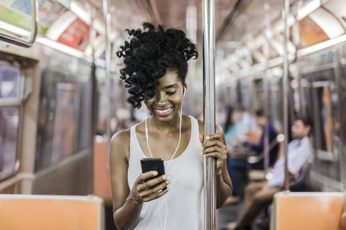 USA, New York City, Manhattan, Porträt einer glücklichen Frau, die im U-Bahn-Zug auf ihr Handy schaut - GIOF02549