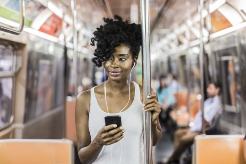 USA, New York City, Manhattan, Porträt einer entspannten Frau mit Mobiltelefon in der U-Bahn, lizenzfreies Stockfoto
