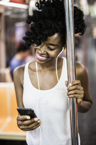 USA, New York City, Manhattan, Porträt einer glücklichen Frau, die im U-Bahn-Zug auf ihr Handy schaut, lizenzfreies Stockfoto