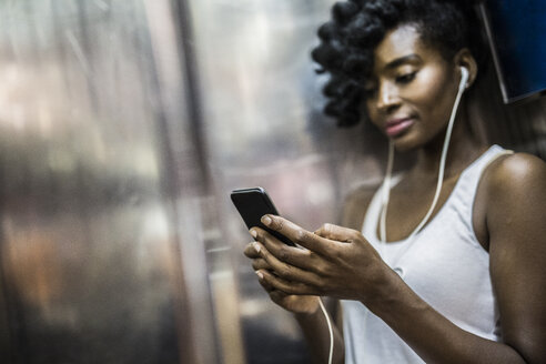 Frau mit Mobiltelefon und Kopfhörern in der U-Bahn - GIOF02553