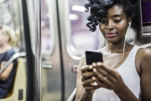 Porträt einer Frau, die im U-Bahn-Zug auf ihr Handy schaut - GIOF02560