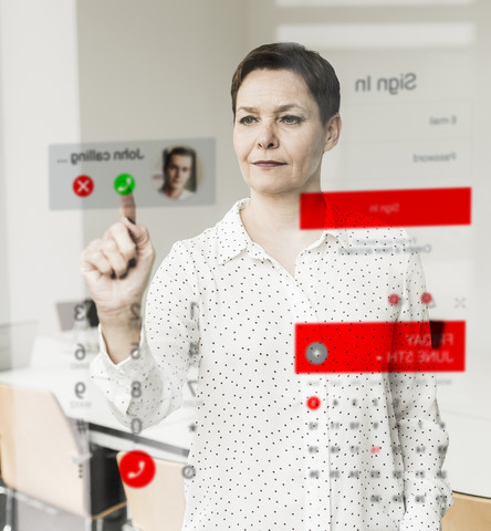 Geschäftsfrau erhält einen Anruf auf einer Glasscheibe im Büro, lizenzfreies Stockfoto