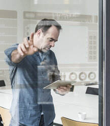 Businessman with tablet touching glass pane with data in office - UUF10240