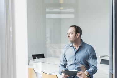 Businessman with tablet looking sideways in office - UUF10259