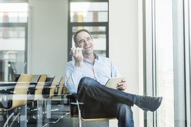 Happy businessman using cell phone and tablet in office - UUF10285