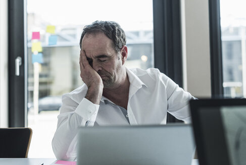 Exhausted businessman sitting at desk in office - UUF10297