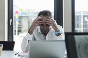 Exhausted businessman sitting at desk in office - UUF10298