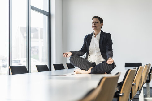 Geschäftsfrau sitzt auf einem Konferenztisch und meditiert - UUF10304