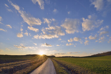 Deutschland, Bayern, Sonnenuntergang mit kleiner Landstraße durch Felder - RUEF01765