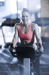 Portrait of smiling woman on spinning bike in gym - ZEF13322