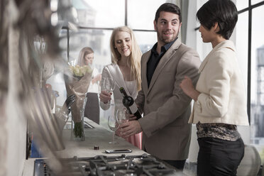 Man with female friends and wine bottle in kitchen - ZEF13359