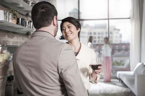 Mann und Frau mit Rotweinglas beim geselligen Beisammensein in einer Stadtwohnung, lizenzfreies Stockfoto
