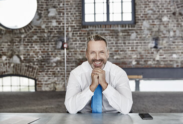 Porträt eines glücklichen Geschäftsmannes, der an einem Tisch in einem Loft sitzt - FMKF03663